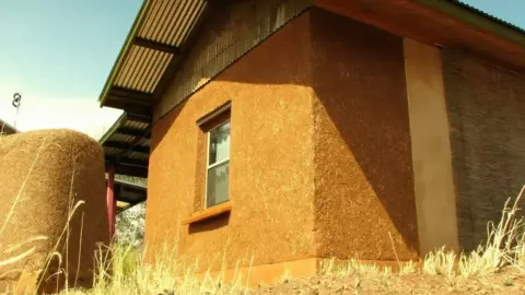 Earthen home with natural plaster walls and generous roof overhangs, showing Dirt Craft Natural Building’s exterior finish in a prairie climate.
